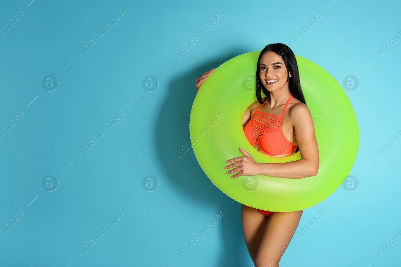 Photo of Beautiful young woman in stylish bikini with green inflatable ring on light blue background. Space for text