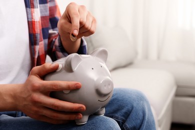 Photo of Man putting coin in piggy bank at home, closeup