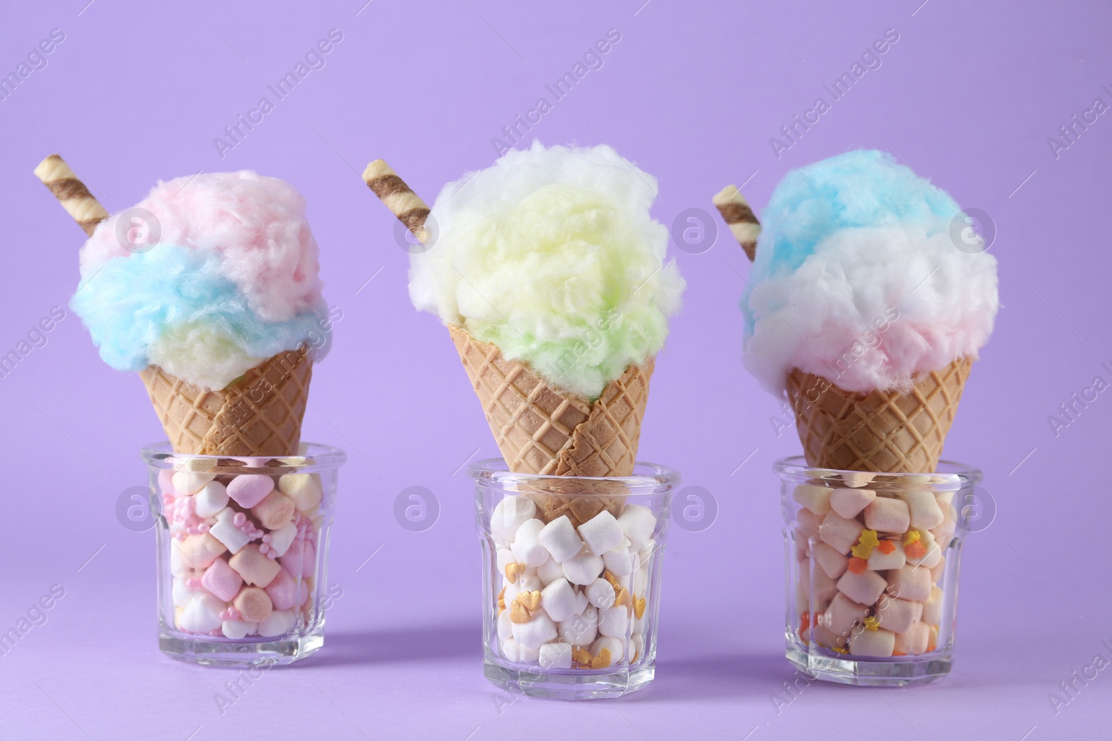 Photo of Sweet cotton candies in waffle cones on purple background, closeup