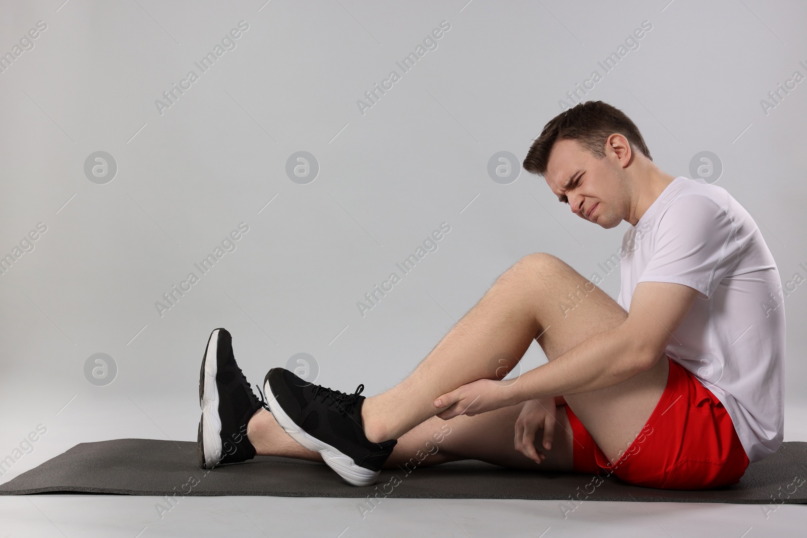 Photo of Man suffering from leg pain on mat against grey background