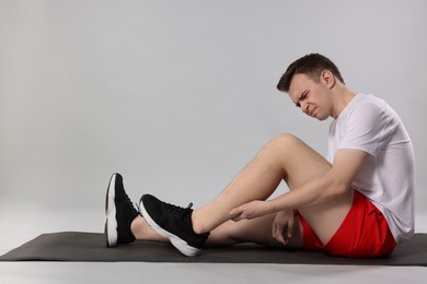 Man suffering from leg pain on mat against grey background