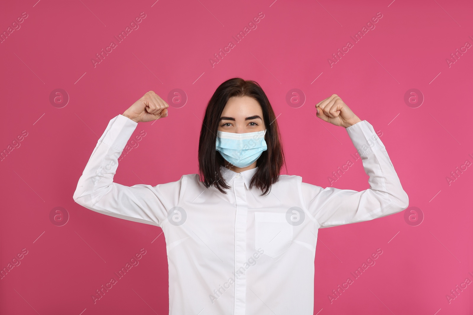 Photo of Woman with protective mask showing muscles on pink background. Strong immunity concept