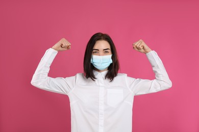 Woman with protective mask showing muscles on pink background. Strong immunity concept
