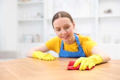 Photo of Woman cleaning wooden table with rag indoors, selective focus