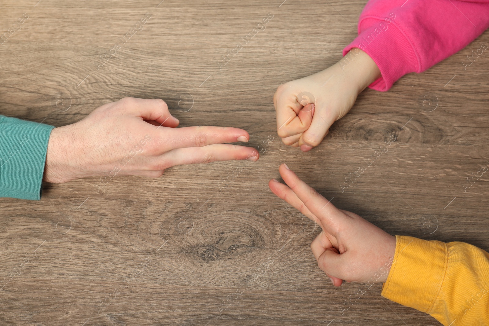 Photo of Closeup of people playing rock, paper and scissors on wooden background, top view