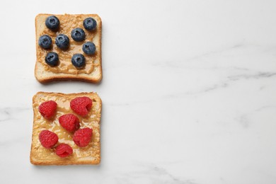 Photo of Delicious toasts with peanut butter, raspberries and blueberries on white marble table, flat lay. Space for text