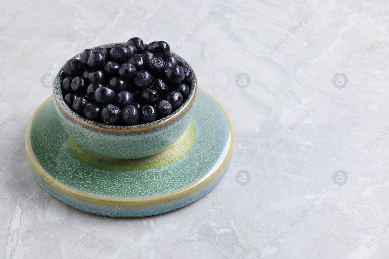 Photo of Tasty fresh bilberries in bowl on light grey marble table, space for text