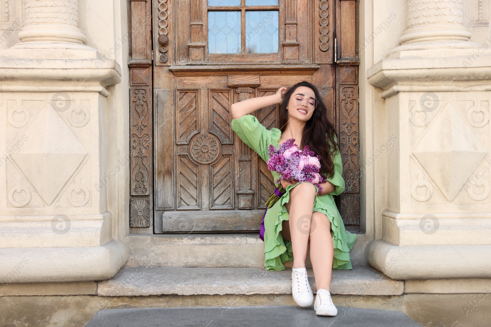 Photo of Beautiful woman with bouquet of spring flowers near building outdoors, space for text