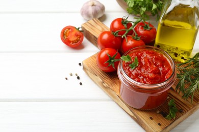 Photo of Homemade tomato sauce in jar and fresh ingredients on white wooden table, space for text