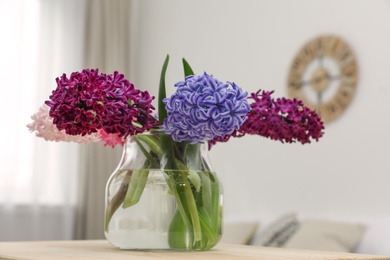 Photo of Beautiful hyacinths in glass vase on table indoors. Spring flowers