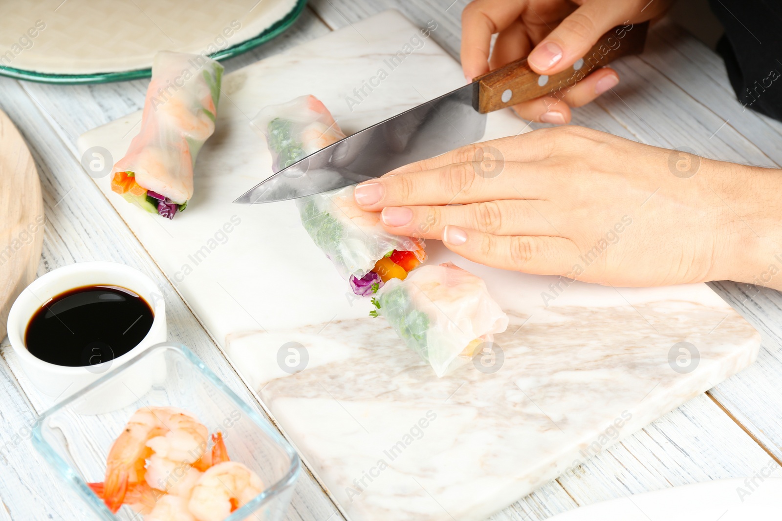 Photo of Woman cutting rice paper roll at white wooden table, closeup