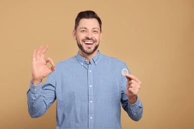 Photo of Happy man with condom showing ok gesture on beige background. Space for text