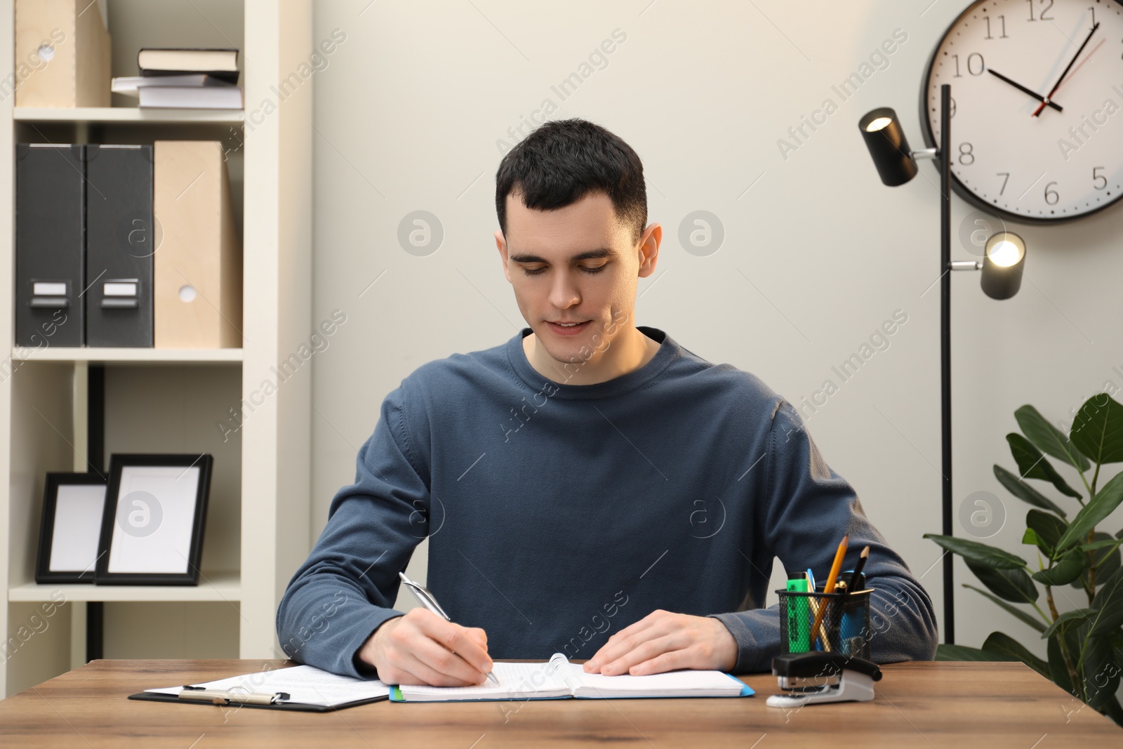 Photo of Man taking notes at wooden table in office