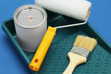Photo of Can of orange paint, brush, roller and container on blue background