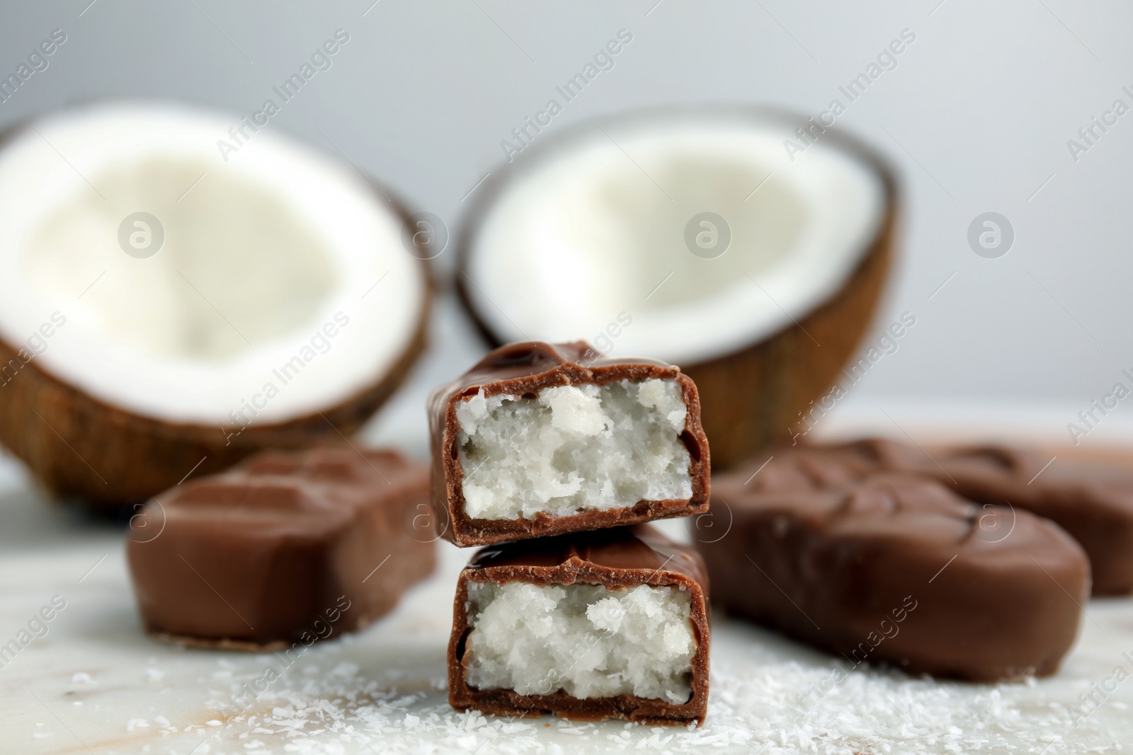 Photo of Delicious milk chocolate candy bars with coconut filling on white table, closeup. Space for text