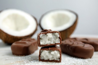 Photo of Delicious milk chocolate candy bars with coconut filling on white table, closeup. Space for text