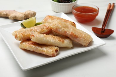 Photo of Tasty fried spring rolls, lime, ginger and sauces on white marble table, closeup