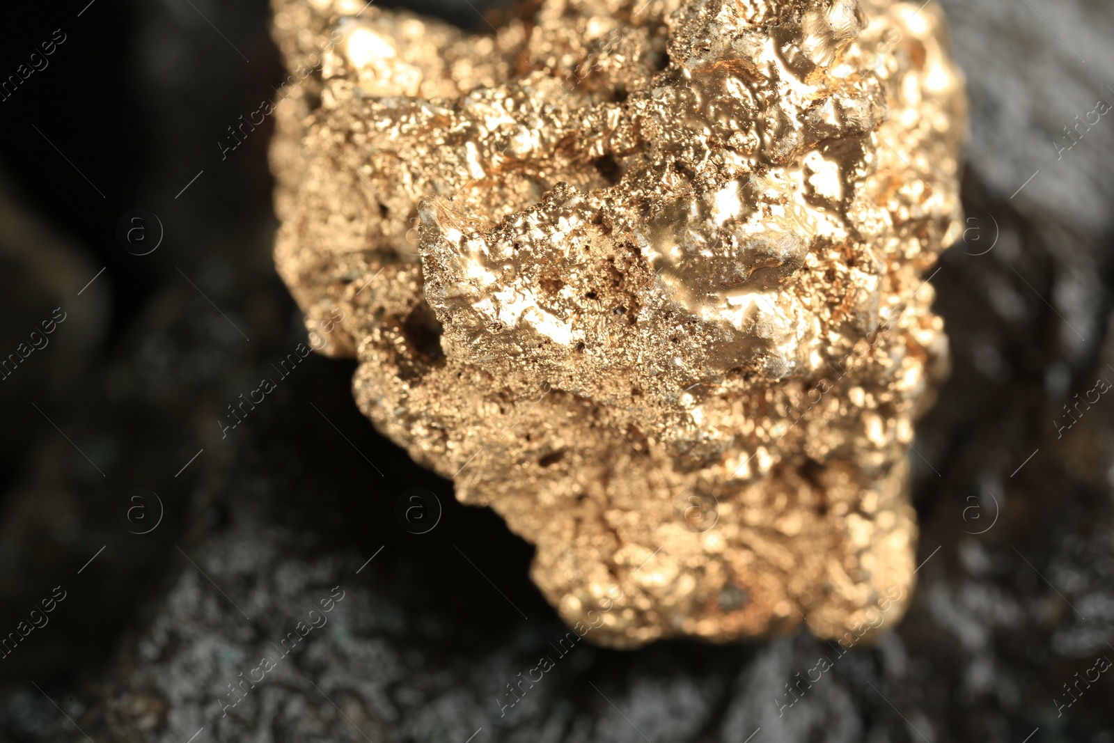 Photo of Shiny gold nugget on grey stone, closeup