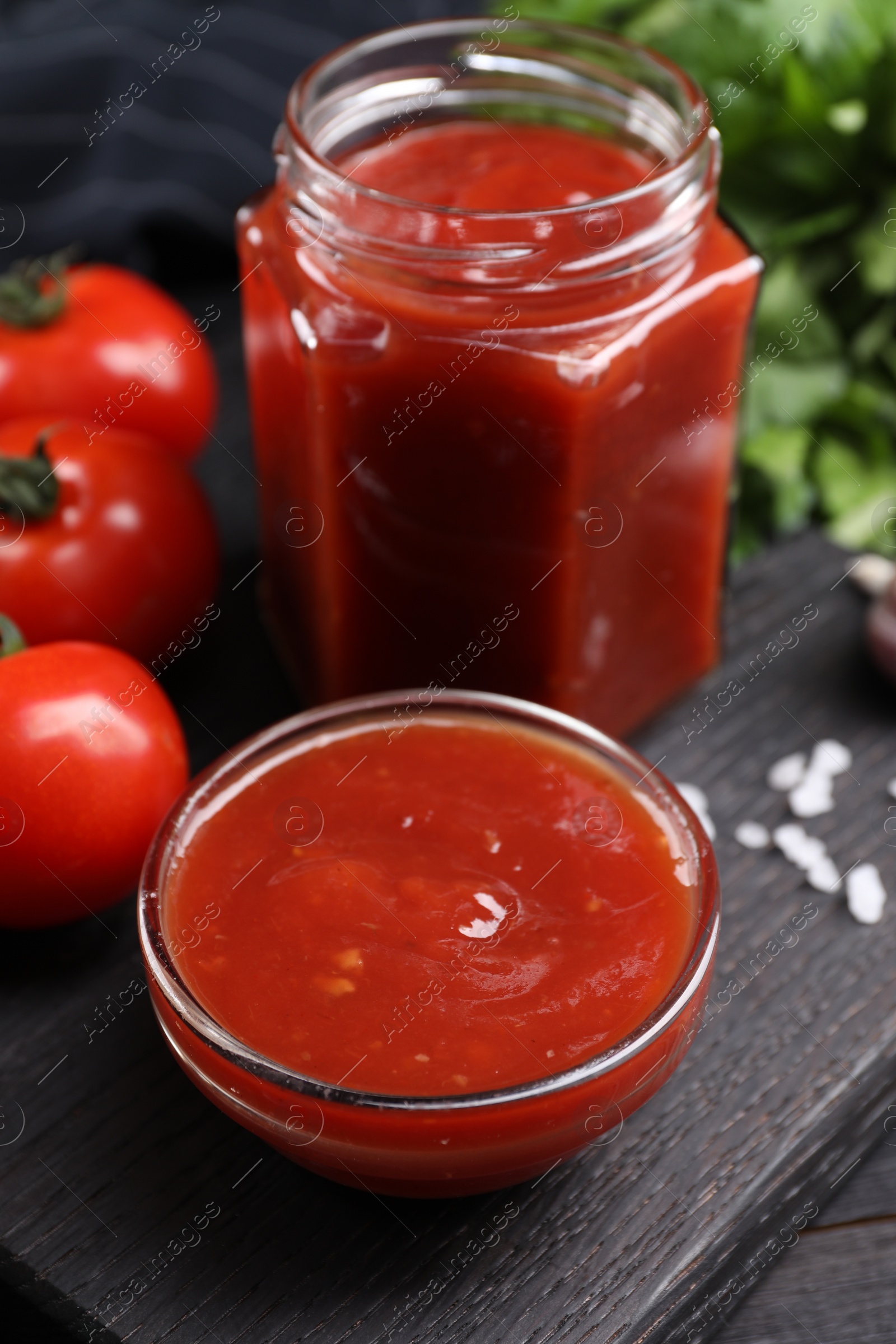 Photo of Delicious ketchup on black wooden table, closeup. Tomato sauce