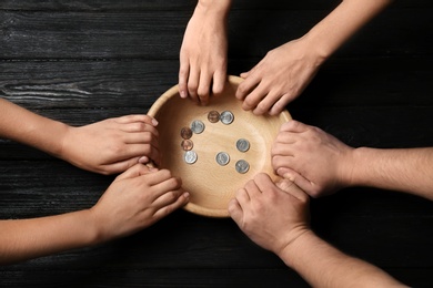 Photo of Poor people holding bowl with coins on wooden background, top view