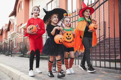 Photo of Cute little kids wearing Halloween costumes going trick-or-treating outdoors