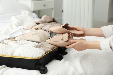Woman holding fashionable shoes near open suitcase in bedroom, closeup