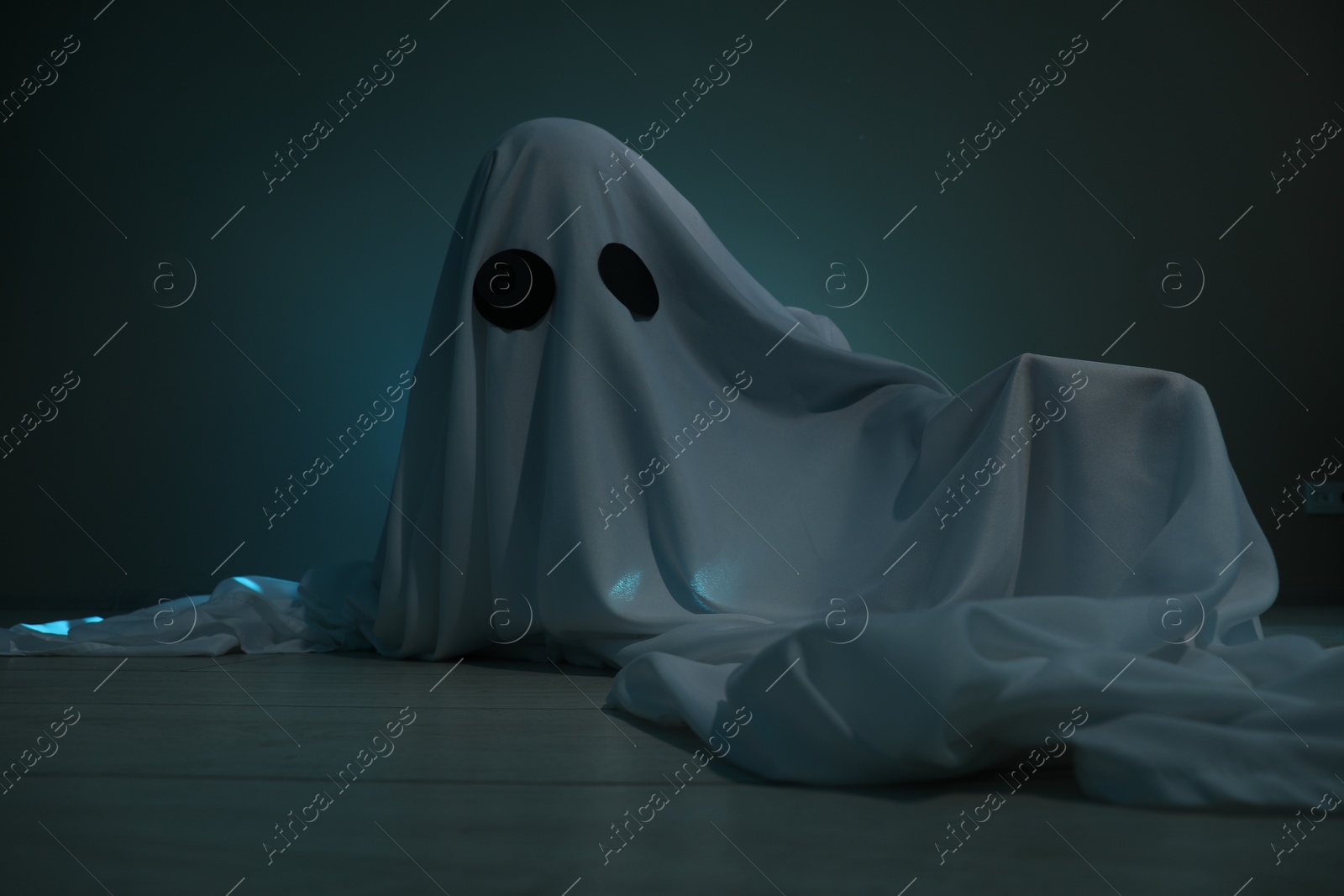 Photo of Creepy ghost. Woman covered with sheet on dark teal background
