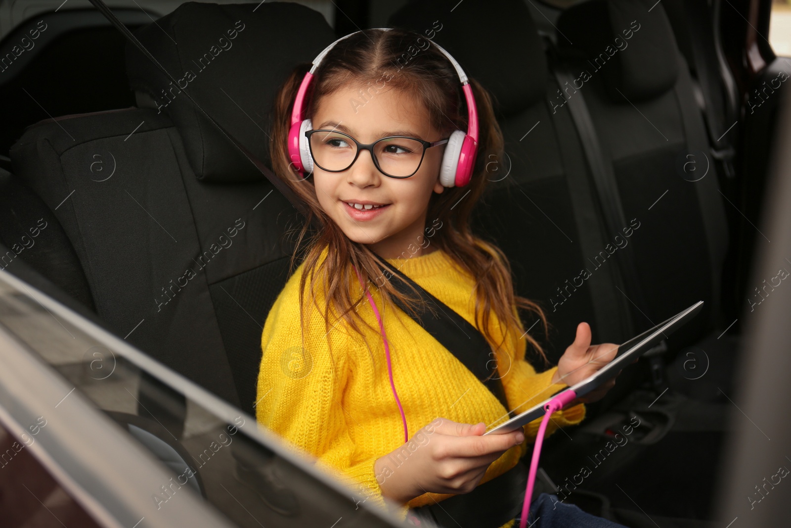 Photo of Cute little girl listening to audiobook in car