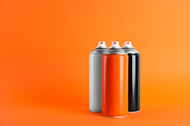Photo of Colorful cans of spray paints on orange background. Space for text