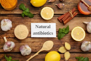 Photo of Different fresh products and card with phrase Natural Antibiotic on wooden table, flat lay