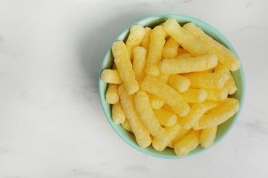 Bowl of delicious crispy corn sticks on white marble table, top view. Space for text