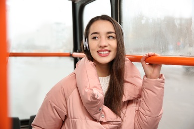 Photo of Beautiful young woman listening to music with headphones in public transport