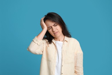 Mature woman suffering from headache on light blue background