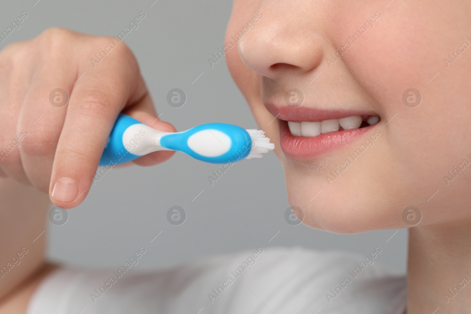 Photo of Girl brushing her teeth with toothbrush on light grey background, closeup