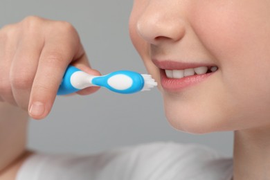 Photo of Girl brushing her teeth with toothbrush on light grey background, closeup