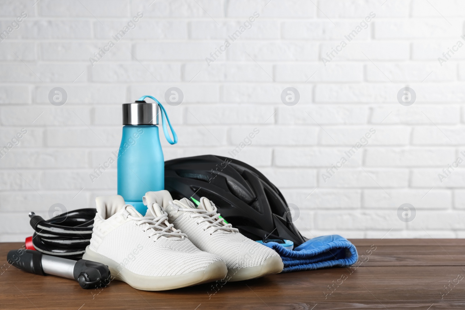 Photo of Different cycling accessories on wooden table against white brick wall, space for text