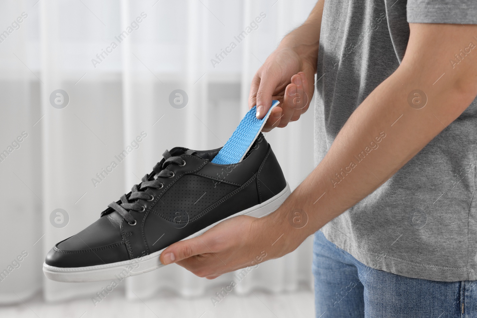 Photo of Man putting orthopedic insole into shoe indoors, closeup