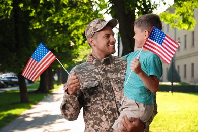 Photo of Soldier and his little son with American flags outdoors. Veterans Day in USA