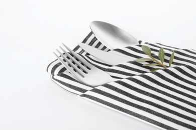 Folded napkin with fork, spoon and knife on white background