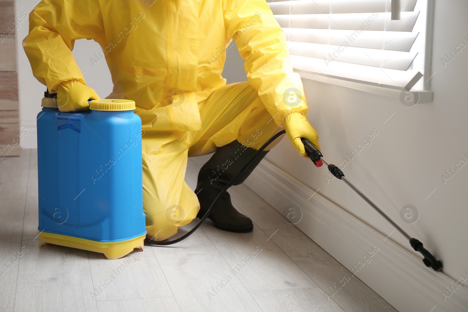 Photo of Pest control worker in protective suit spraying pesticide near window indoors, closeup