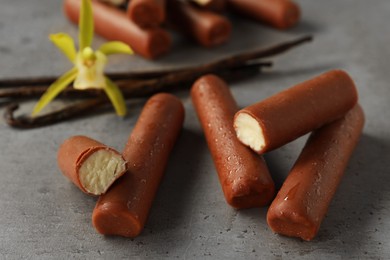 Photo of Glazed curd cheese bars, vanilla pods and flower on grey table, closeup