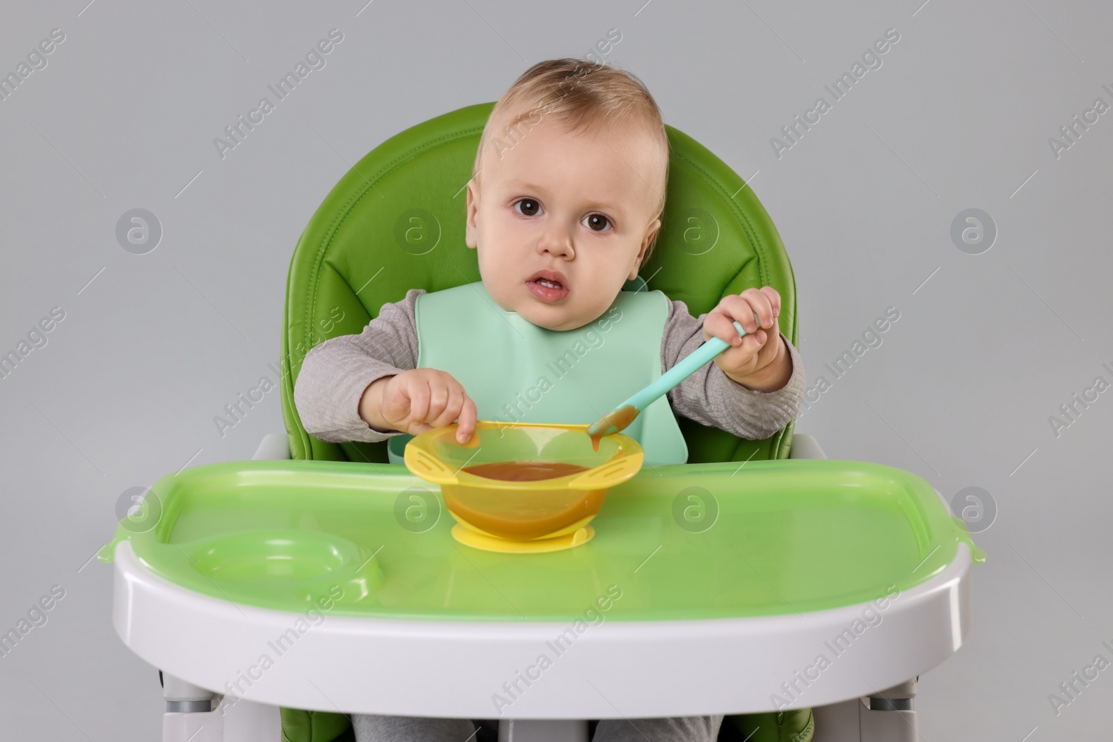 Photo of Cute little baby eating healthy food in high chair on gray background