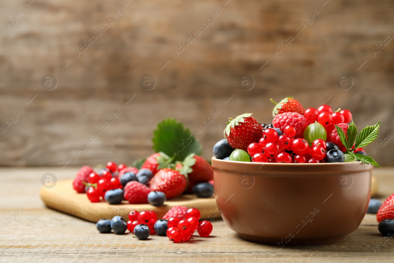 Photo of Mix of different fresh berries in bowl on wooden table. Space for text