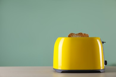 Photo of Modern toaster with slices of roasted bread on wooden table. Space for text