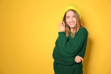 Image of Happy young woman wearing warm sweater and knitted hat on yellow background. Space for text