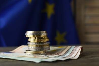 Photo of Stack of coins and banknotes on wooden table against European Union flag, space for text