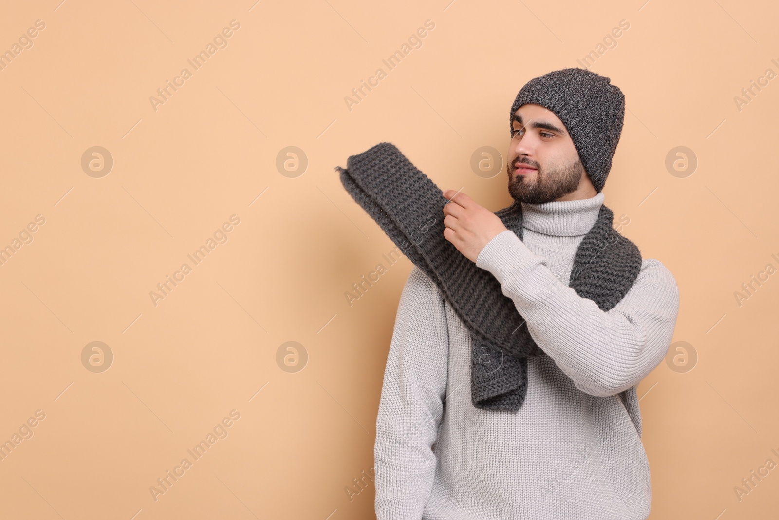 Photo of Handsome man in knitted scarf and hat on beige background. Space for text
