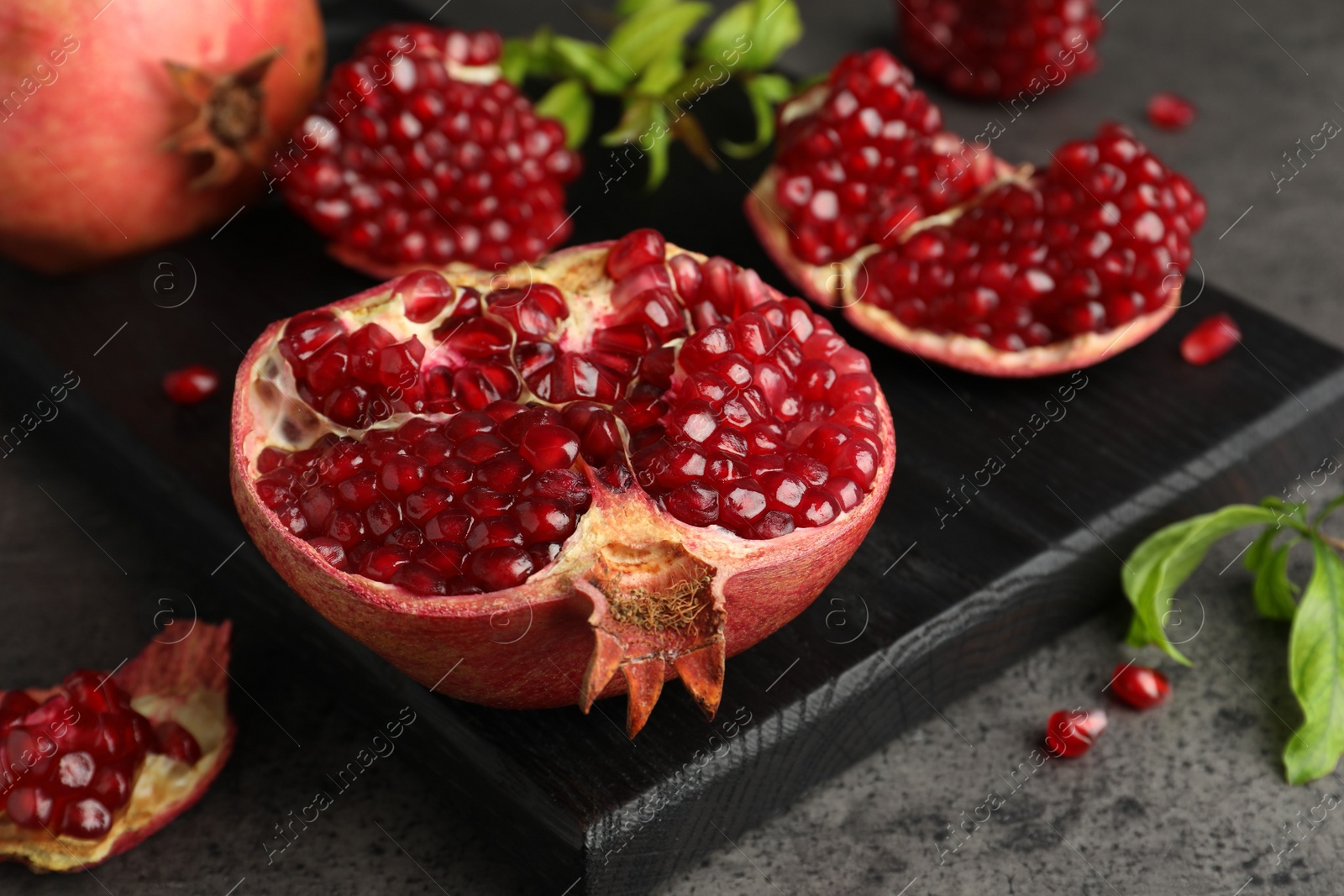 Photo of Cut fresh pomegranate and green leaves on grey table, closeup