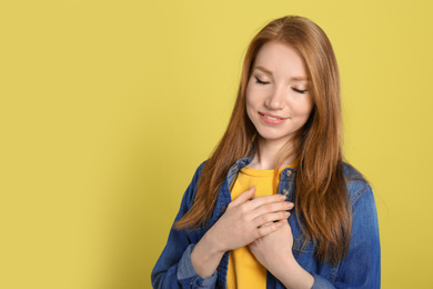 Photo of Beautiful grateful woman with hands on chest against yellow background. Space for text