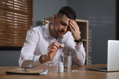 Photo of Man taking medicine for hangover at desk in office